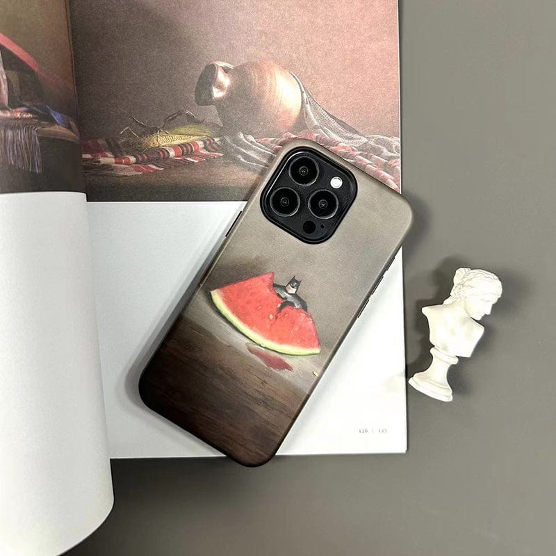 A smartphone with the Quirky Watermelon & Miniature Hero iPhone 16 Pro Max Case - Fun and Unique Design, Ultra-Slim, Full Protection, featuring an image of a cat wearing a small cape standing on a slice of watermelon, rests on an open book with a still life painting, next to a small white bust sculpture.