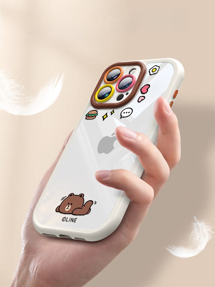 A person is holding the iPhone 16 Pro Max Case - Cute Cartoon Clear Protective Cover with Shockproof Bumper and Anti-Yellowing Transparent Back, adorned with a playful cartoon design featuring a bear, food items, and thought bubble stickers on its white finish.