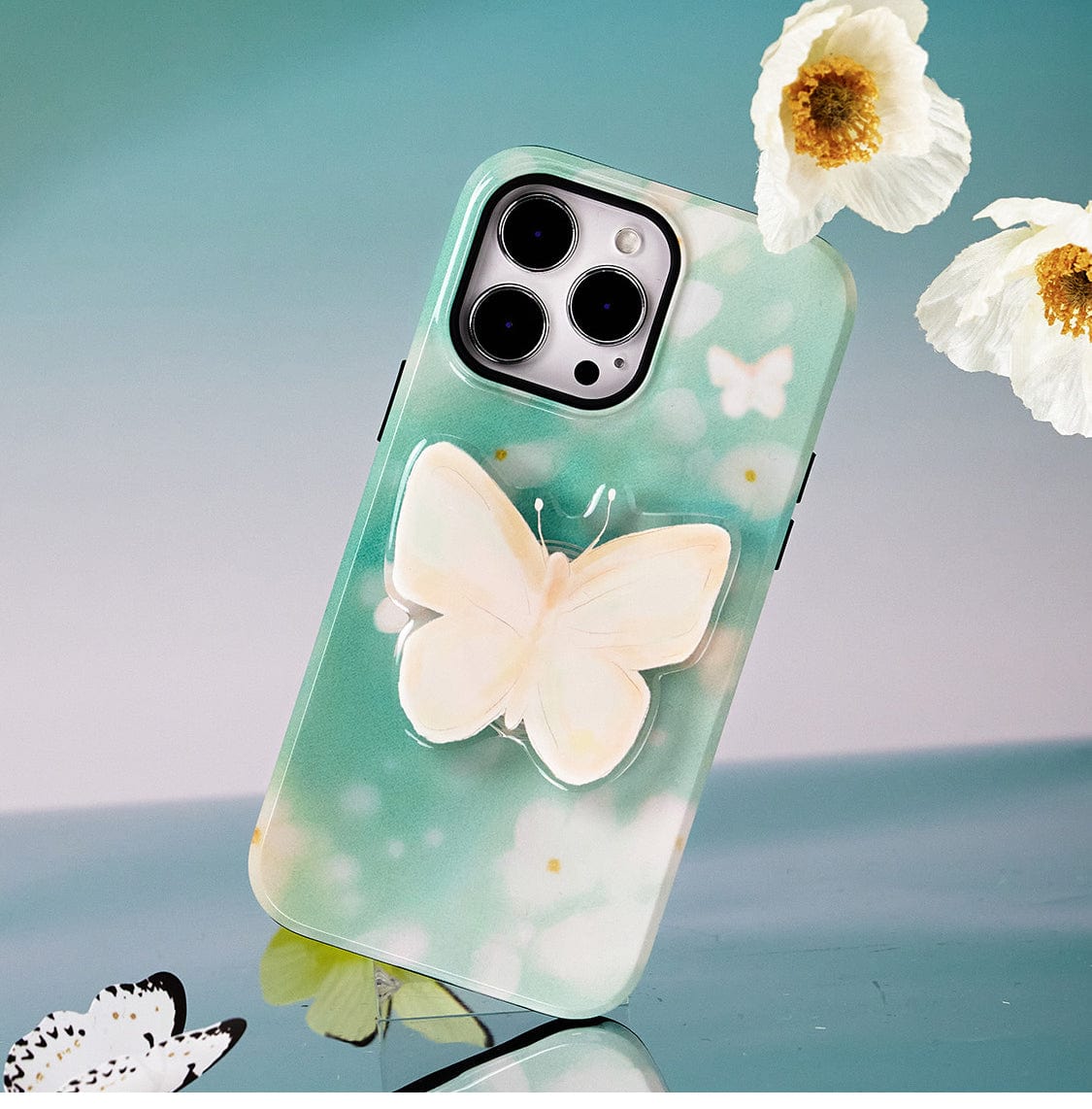 A Butterfly Blossom MagSafe iPhone 16 Pro Max Case, showcasing an elegant floral design and butterfly-themed motif, holds the smartphone positioned sideways next to white flowers.