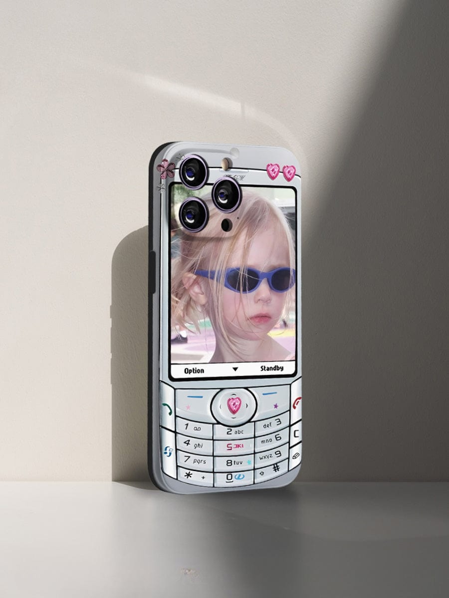 A modern smartphone with a Retro Flip Phone iPhone 16 Pro Max Case—featuring a Y2K Nostalgia Design and fun, all-inclusive protective cover—displays a young girl wearing sunglasses on its screen. The case is adorned with keypad buttons and heart-shaped decorations.