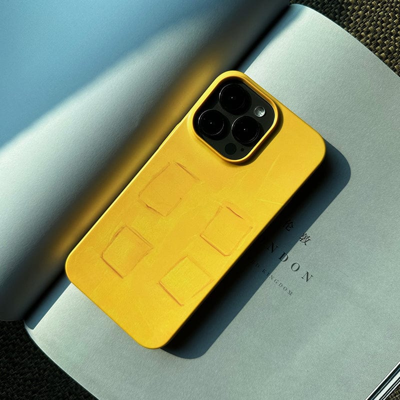 A smartphone with a Bold Yellow Textured iPhone 16 Pro Max Case - Modern Art, Minimalist Design, and Durable Protection is lying on an open book. The sunny lighting casts clear shadows and highlights the texture of the yellow cover. The book has some text visible, but it is partially obscured by the phone.