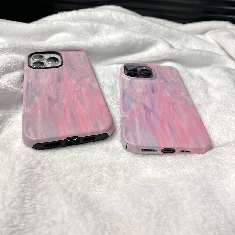 Two smartphones with pastel pink and blue marble-patterned cases are lying on a soft, white fabric. One phone, featuring the Pastel Brushstrokes iPhone 16 Pro Max Case - Soft Artistic Design with Full Protection, is slightly larger than the other. Both phones are placed face down, showcasing the distinctive swirl designs of their cases.