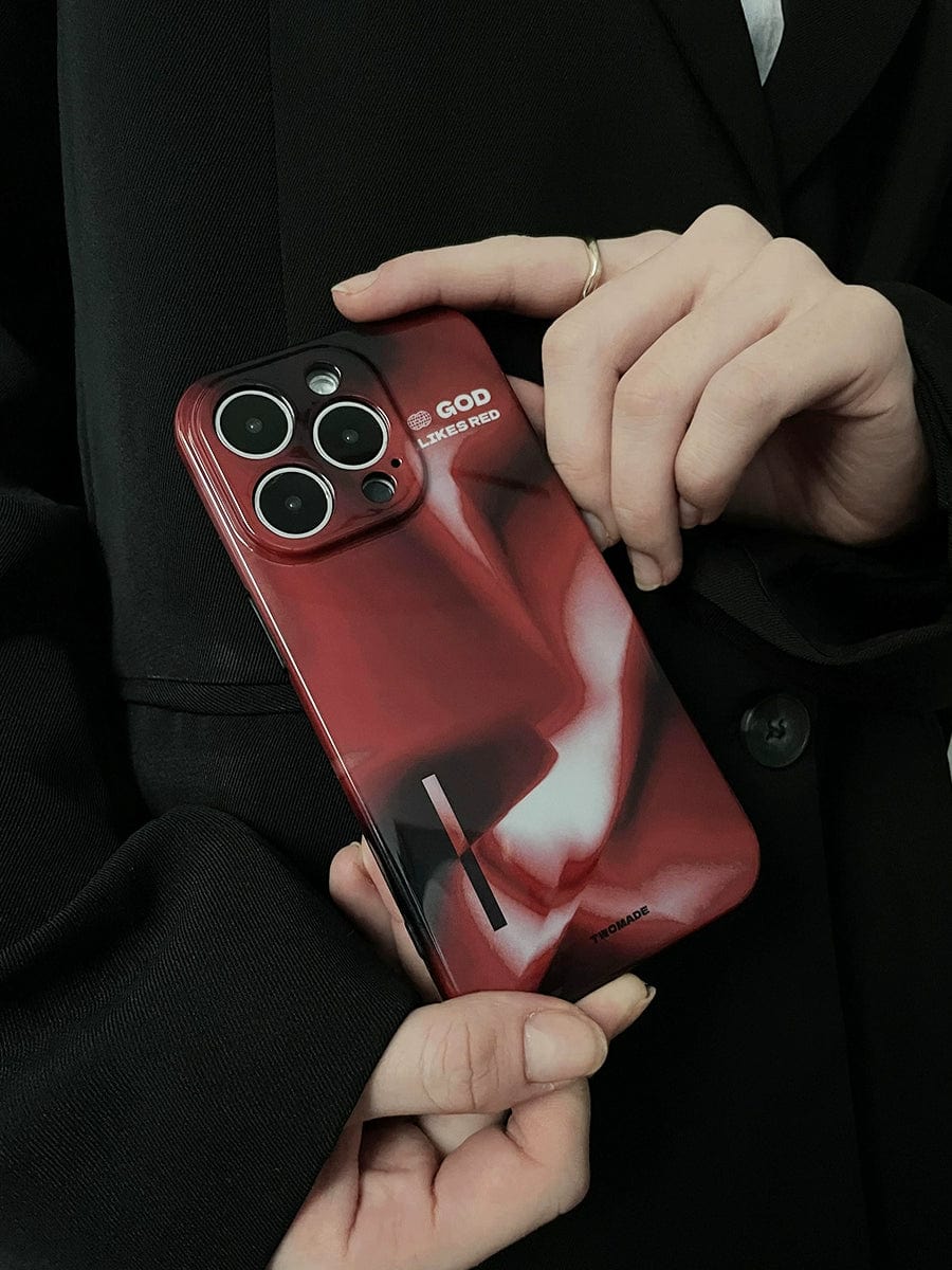 A person wearing a black blazer holds a smartphone with the God Likes Red iPhone 16 Pro Max Case. The phone, equipped with three camera lenses, is encased in a premium all-inclusive protective cover featuring bold abstract art, white text that reads "GOD," and smaller text saying "LEAVE ME RED.