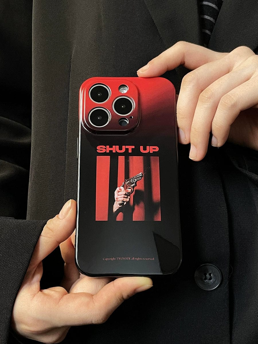 Close-up of a person holding the Shut Up Red Gradient iPhone 16 Pro Max Case. The custom case features a red and black design depicting a hand holding a gun, with the text "SHUT UP" in bold red letters above the image. The person's hands and part of a black coat are visible.