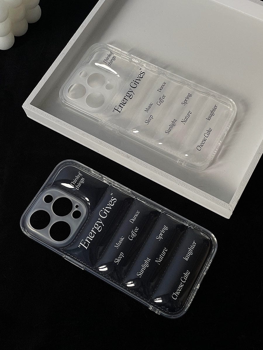 The black surface showcases two transparent iPhone 16 Pro Max cases. One is presented in a white tray, and both feature the "Energy Gives" label along with sources of positive energy such as "Sunlight" and "Music." These Energy Gives iPhone 16 Pro Max Cases with their clear, motivational design could be the perfect way to brighten your day.