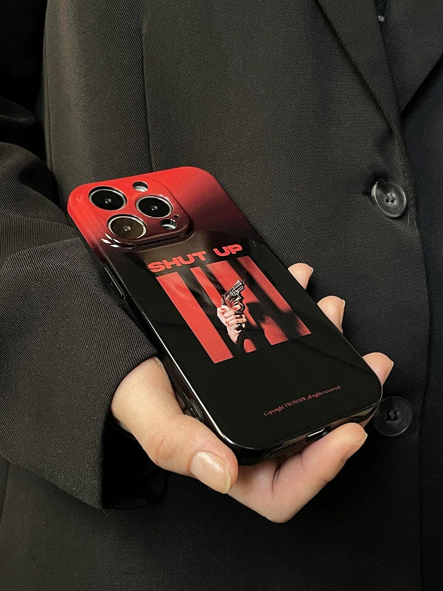 A person in a black jacket holds a phone with the "Shut Up Red Gradient iPhone 16 Pro Max Case | Bold Statement Design | All-Inclusive Protective Cover," which features a striking red and black design with an image of a hand holding a gun and the text "SHUT UP.