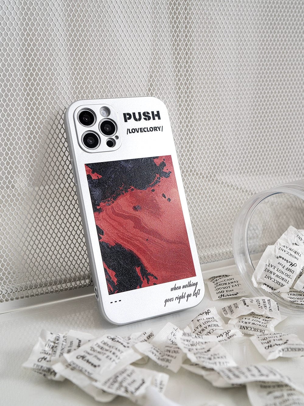 A PUSH LoveGlory iPhone 16 Pro Max Case, boasting a bold artistic black and red abstract design with the motivational phrases "PUSH LOVECLOXY" and "when nothing goes right go left," is displayed on a mesh background surrounded by crumpled paper pieces.