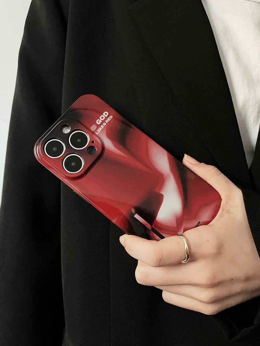 A person dressed in a black blazer and white shirt is holding an iPhone 16 Pro Max encased in the "God Likes Red" iPhone 16 Pro Max Case, featuring a bold abstract design. The phone showcases its triple rear cameras, while a ring on their index finger is also visible.