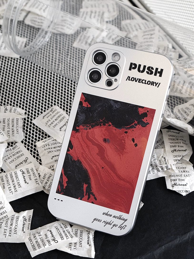 The PUSH LoveGlory iPhone 16 Pro Max Case, adorned in white with bold abstract red and black artwork, lies amidst a spread of silica gel packets. The case features the words "PUSH" and "LOVEGLORY," along with the inspiring caption: "when nothing goes right go left.