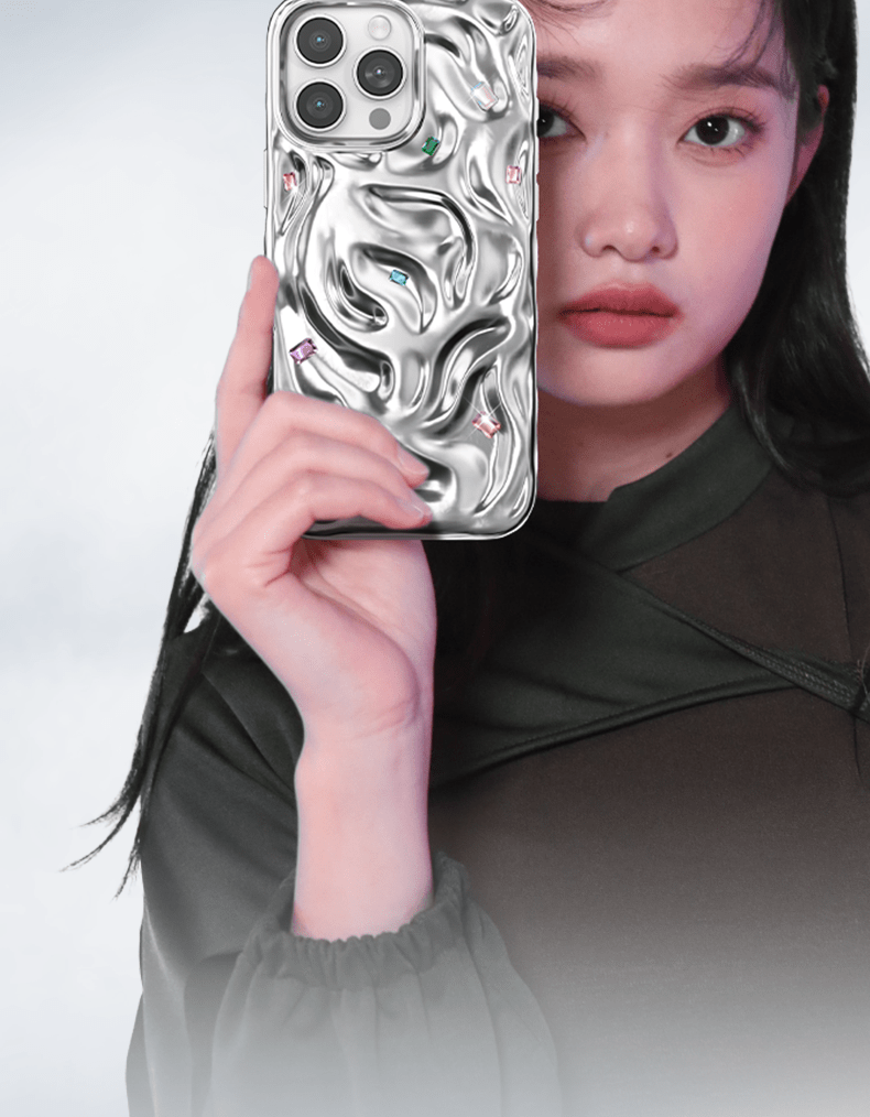 A person holding an iPhone 16 Pro Max Luxury Case featuring a silver, textured design with handcrafted gemstone detailing is covering part of their face.