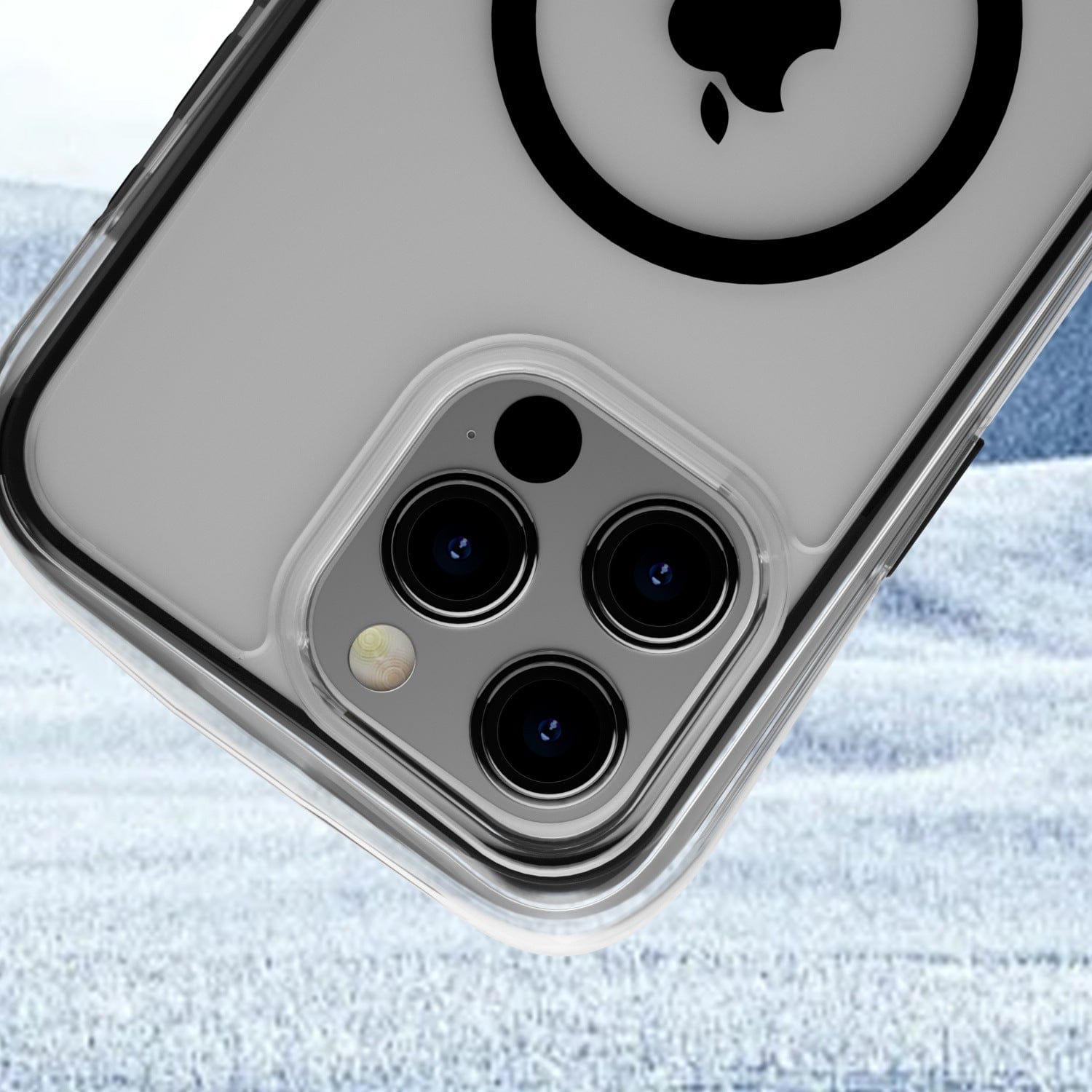 Close-up of the back of an iPhone 16 Pro Max in a 360° Shockproof Clear Protective Cover from the Air Cushion MagSafe Case line, showing three camera lenses and an Apple logo against a snowy background.