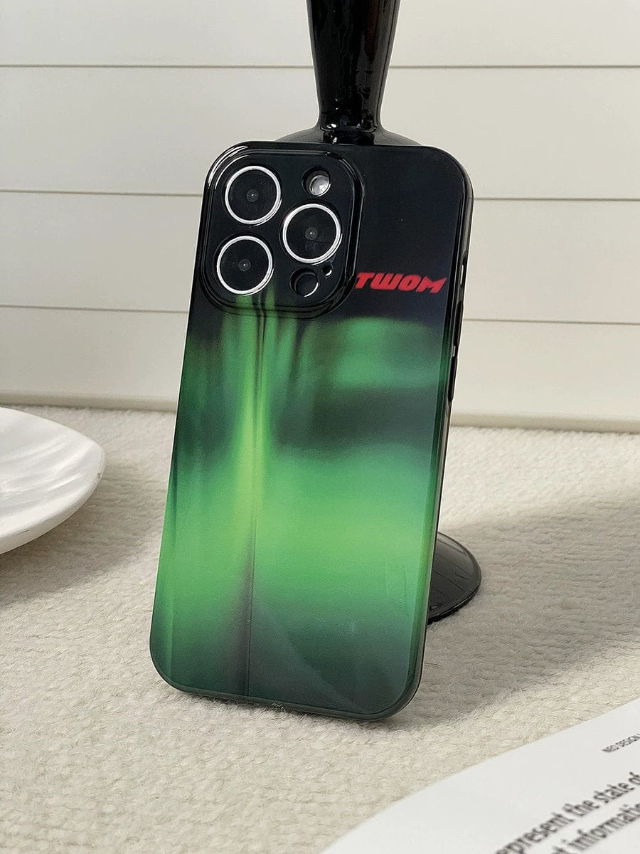 A dark-colored iPhone 16 Pro Max, encased in an Aurora Green Gradient case with a sleek Northern Lights design and featuring three camera lenses, rests against a black stand on a light-colored surface.