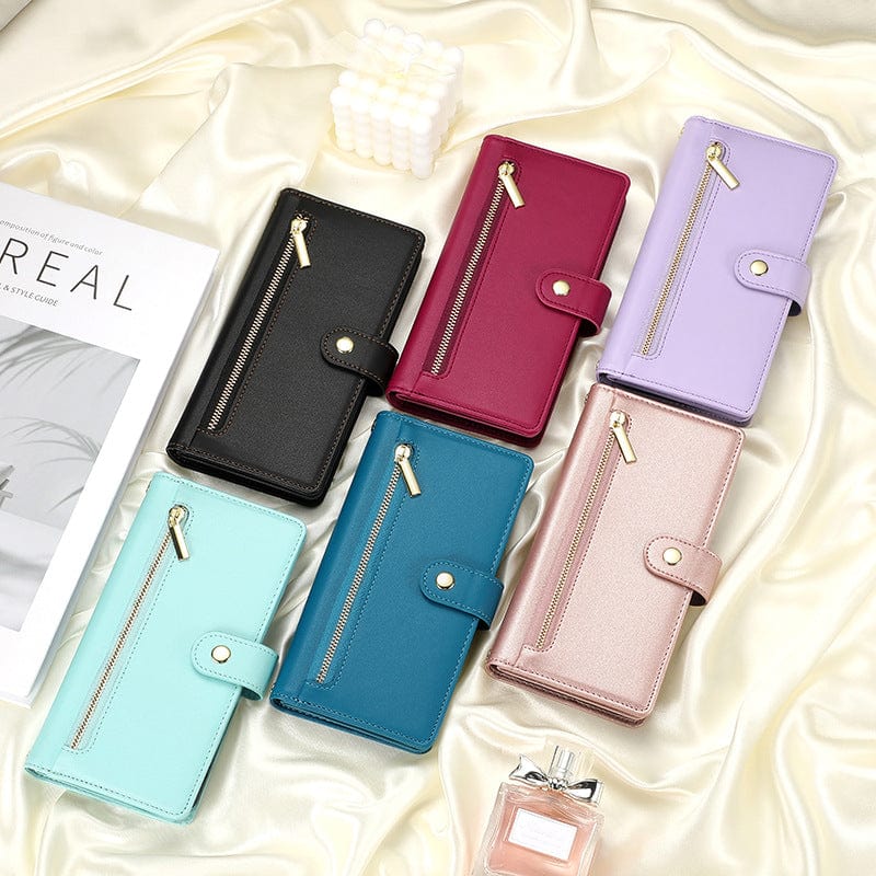 Six iPhone 16 Pro Max Wallet Cases, available in a palette of black, red, purple, turquoise, blue, and beige leather folio covers, are elegantly laid out on a satin surface next to a magazine and a perfume bottle. Each case is meticulously crafted from premium leather and includes features such as a card holder pocket with both zipper and snap closures.