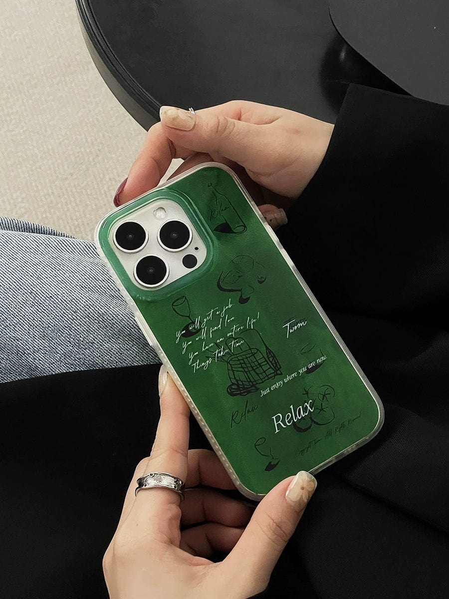 Close-up of hands holding a smartphone, specifically an iPhone 16 Pro Max in a Relax Green iPhone 16 Pro Max Case featuring artistic minimalist designs and motivational text. Denim pants and black fabric create a stylish background.