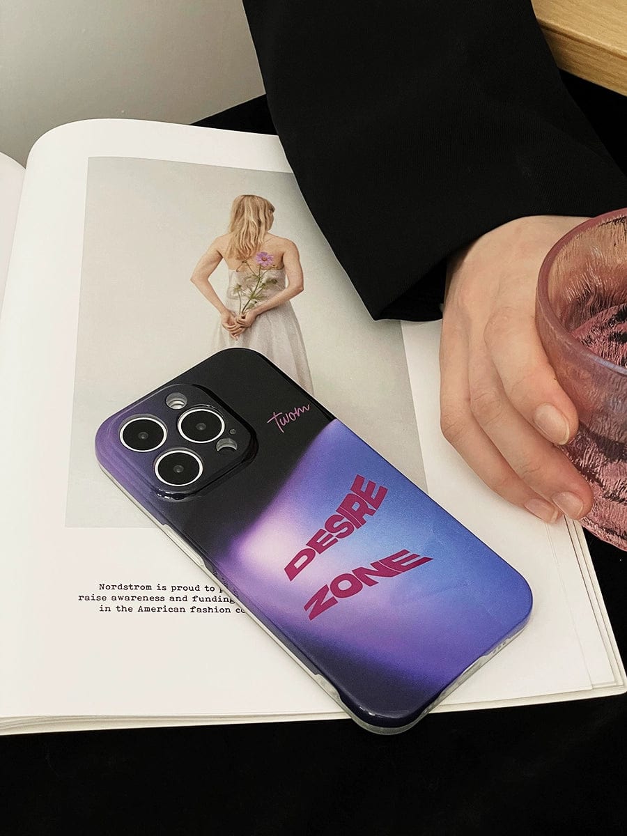 A smartphone with a Desire Zone iPhone 16 Pro Max Case, featuring a Gradient Urban Style and Sleek All-Inclusive Protective Cover, rests on an open magazine displaying a woman in a white dress holding flowers. Beside the phone, a hand holds a pink glass, while the background reveals a black garment likely worn by the hand's owner.