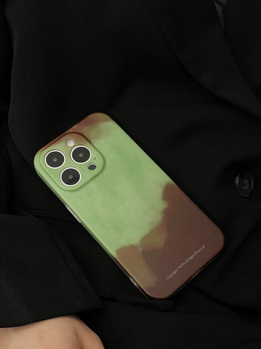 A person in a dark jacket, visible from the shoulders down, is holding an iPhone 16 Pro Max fitted with a Midnight Galaxy iPhone 16 Pro Max Case featuring a cosmic starry design in green and brown. The phone showcases three camera lenses and a flash, while white text is printed on the bottom edge of the premium all-inclusive protective cover.