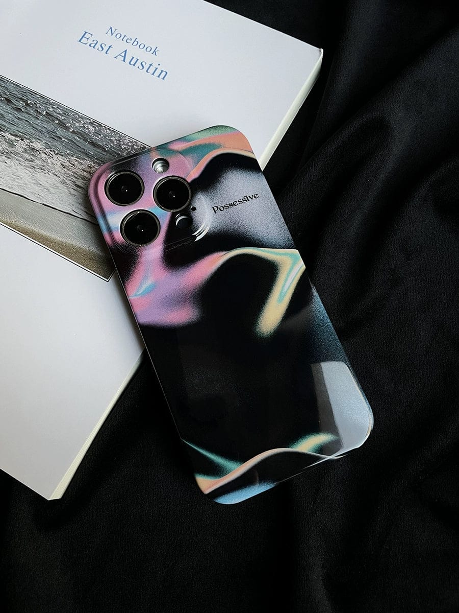 A smartphone with a Possessive Aura iPhone 16 Pro Max Case featuring an abstract fluid design rests on an open notebook titled "East Austin." The background is a black fabric, creating a striking contrast with the vibrant phone case and the white notebook page visible beside it.