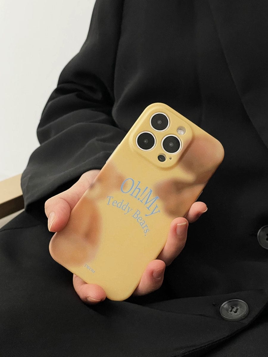 A person wearing a black coat holds an Oh! My Teddy Bears iPhone 16 Pro Max case, featuring a yellow design with the text "Oh My Teddy Bears" and an image of teddy bears in the background.