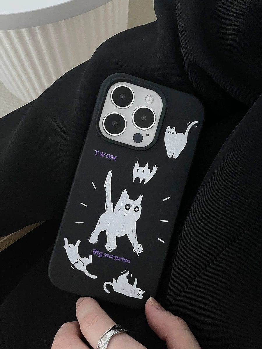 A hand is holding a Big Surprise Black Cat iPhone 16 Pro Max case with a playful cartoon design depicting four white cats in various poses. The case also features the words "TWOM" and "Big surprise!" in purple text. The background of the image appears dark.