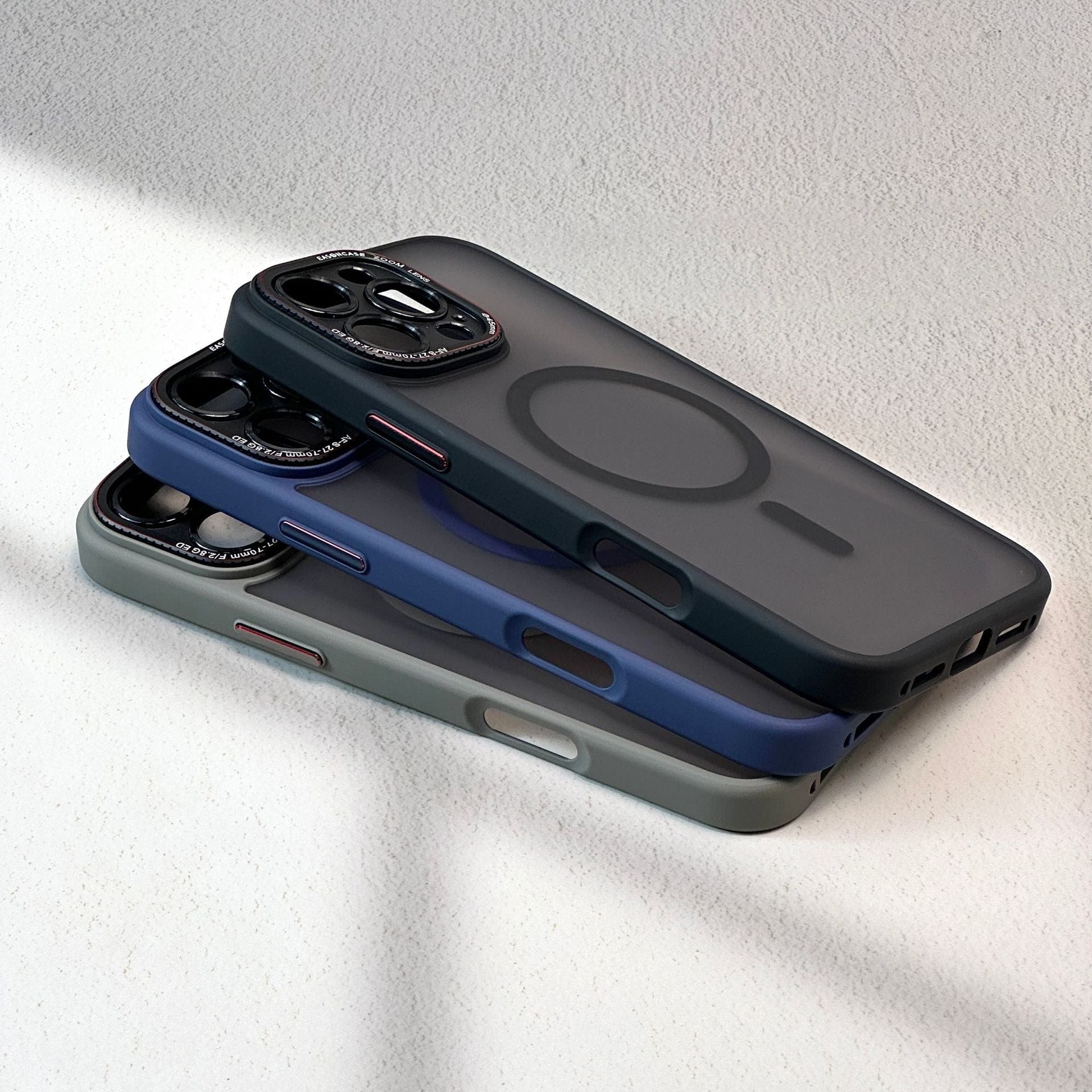 Three smartphones with cases in black, blue, and gray stacked on top of each other, showcasing the rear camera setups and MagSafe ring designs of the iPhone 16 Pro Max Case - Matte Finish, Shockproof Full-Coverage with MagSafe Compatibility.