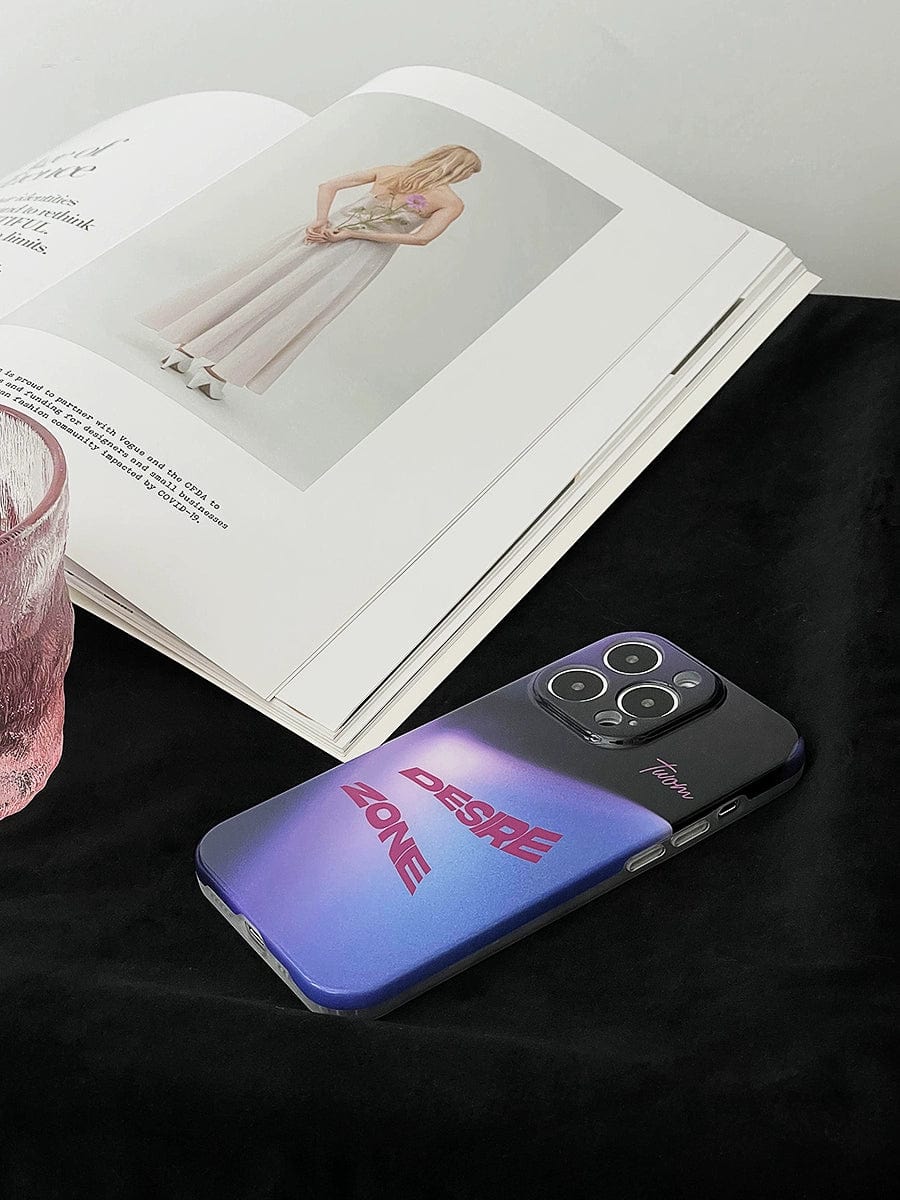 A smartphone with a Desire Zone iPhone 16 Pro Max Case featuring a sleek, gradient urban style rests on a black surface. Beside it is an open book displaying an image of a person in a light-colored dress. A pink glass sits to the left.