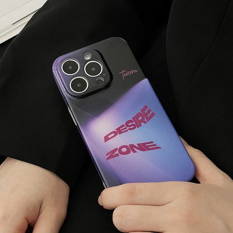 A person holding an iPhone 16 Pro Max with the Desire Zone iPhone 16 Pro Max Case — a sleek, all-inclusive protective cover featuring a gradient urban style in shades of purple and blue, adorned with "DESIRE ZONE" in bold pink letters and the word "team" near the camera lenses. The person is dressed in black clothing.