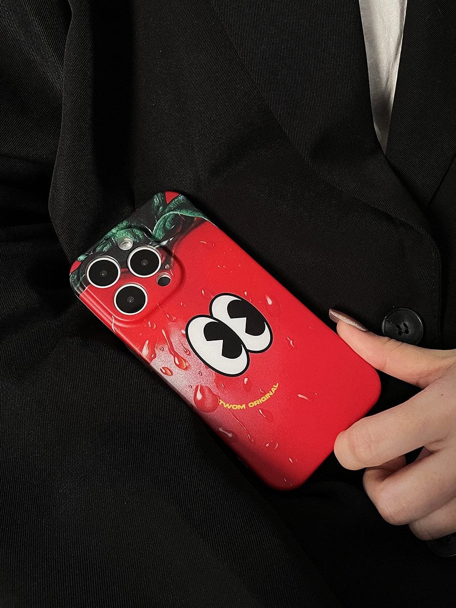 A hand holds an iPhone 16 Pro Max in a Tomato Face iPhone 16 Pro Max Case, featuring a whimsical red cartoon design with googly eyes and water droplets, over a dark blazer.