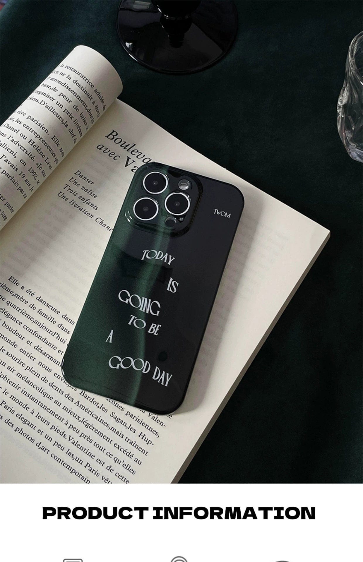 A smartphone with a "Good Day Quote iPhone 16 Pro Max Case," featuring a sleek dark green design and motivational message, rests on an open book. The background is dark, and a glass and candle are visible.