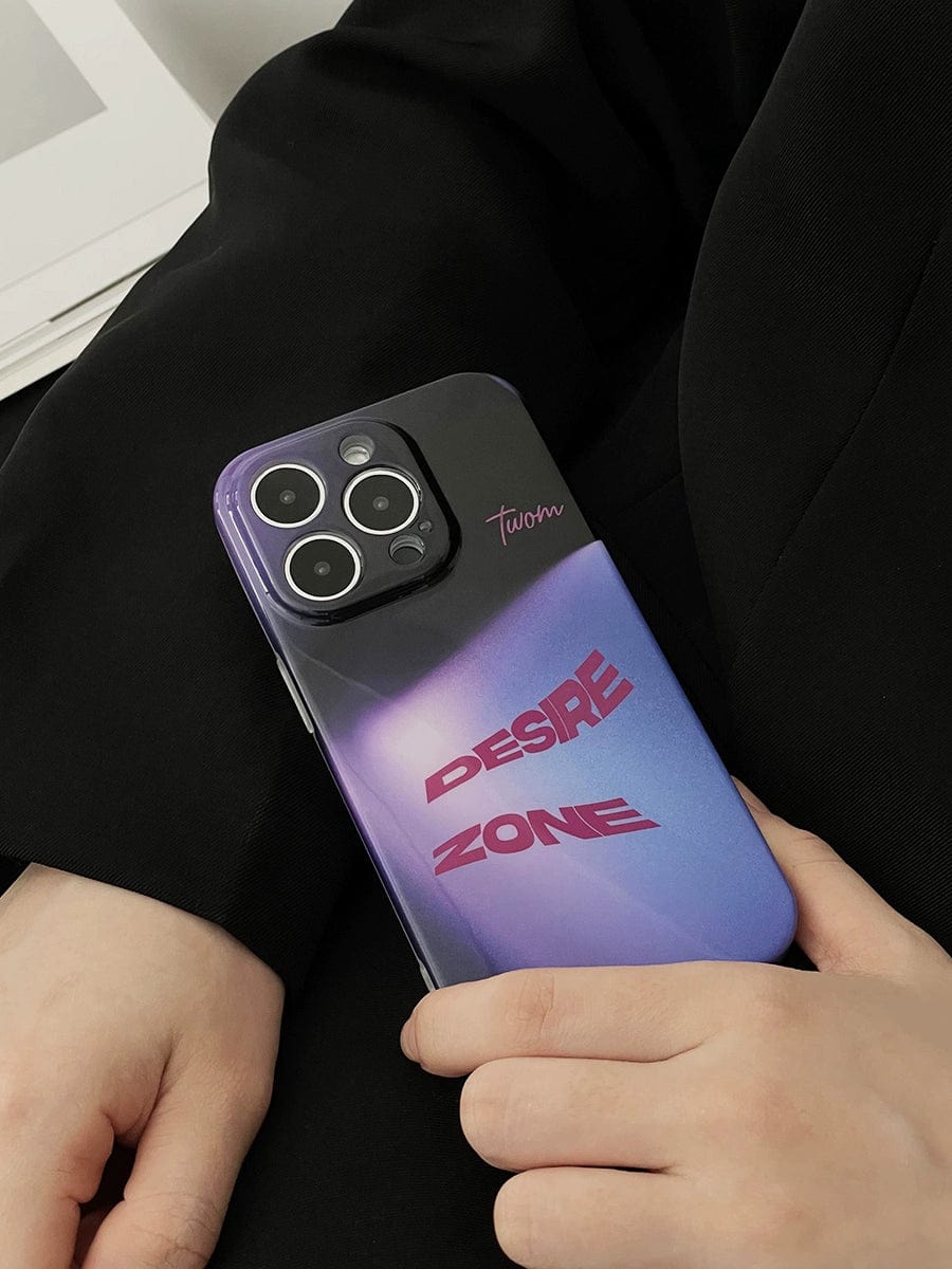 A close-up of a person holding the Desire Zone iPhone 16 Pro Max Case with a dual-tone purple and black design. The case features the words "DESIRE ZONE" in bold, purple font and includes a signature or logo reading "twom" near the cameras at the back. The person is dressed in black.