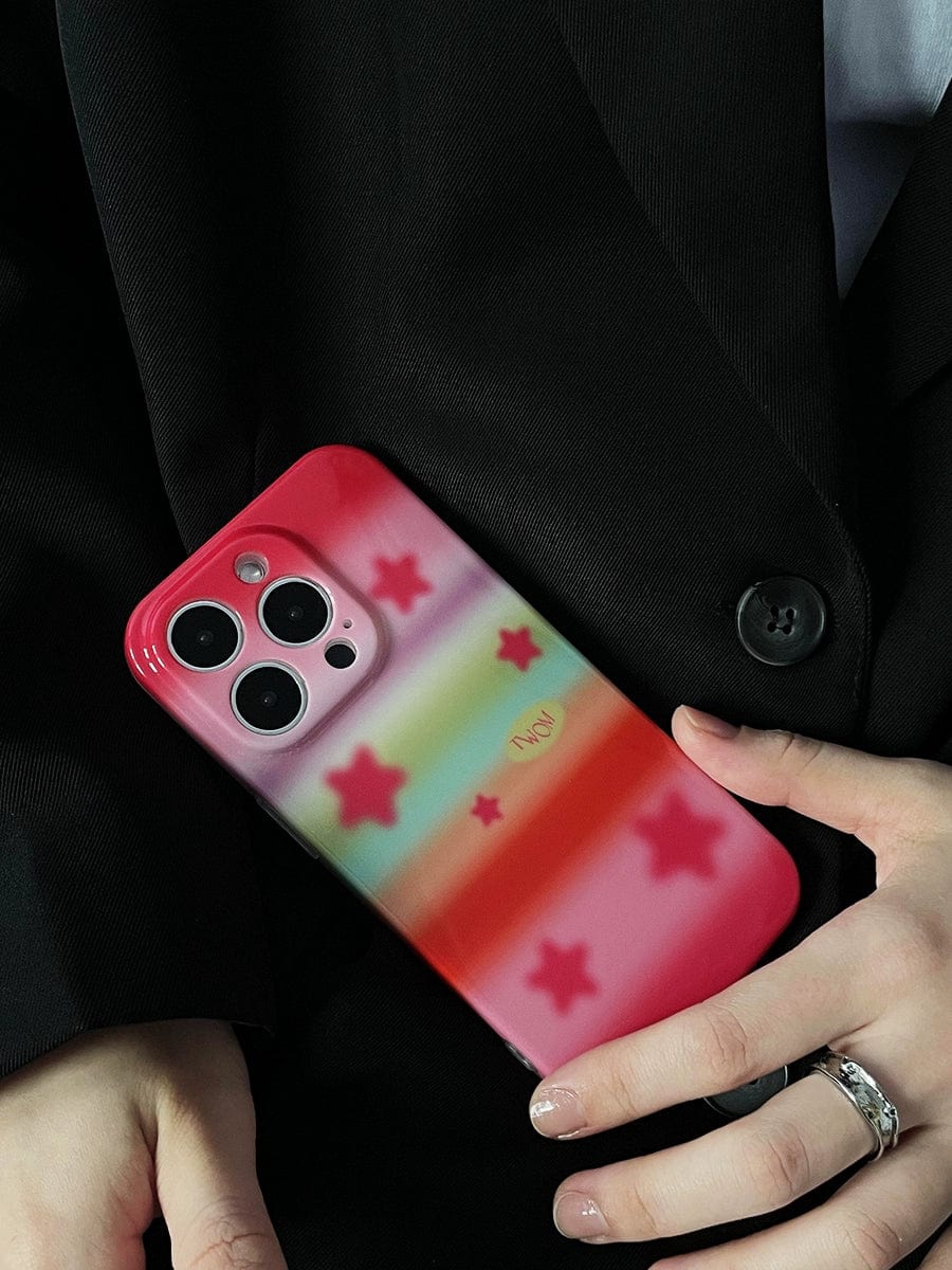 Person holding an iPhone 16 Pro Max in a Pink Starburst iPhone 16 Pro Max Case with a pastel rainbow design, wearing a black blazer.