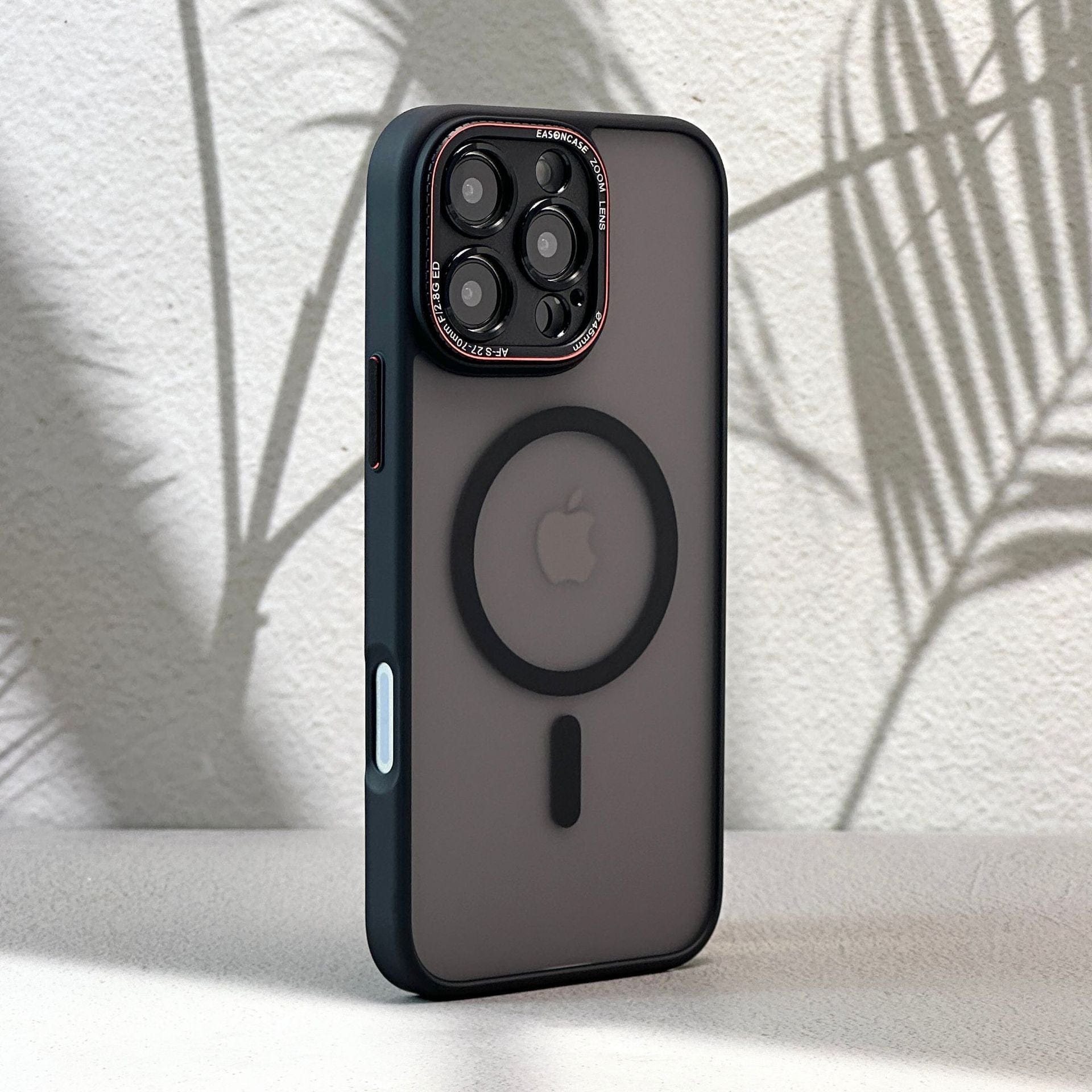 An iPhone 16 Pro Max Case - Matte Finish, Shockproof Full-Coverage with MagSafe Compatibility in sleek black, featuring a circular design on the back, is placed on a light surface with blurred shadows of leaves in the background.