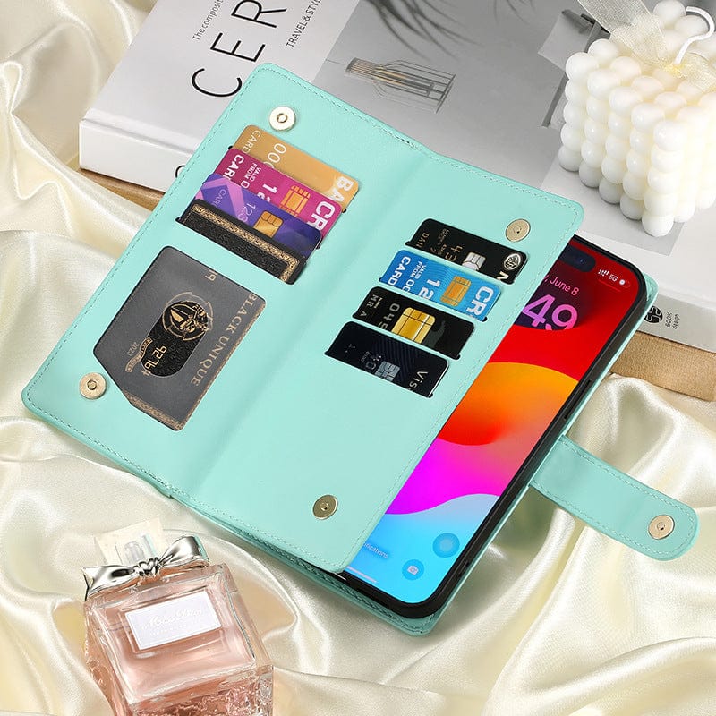 Open iPhone 16 Pro Max Wallet Case with Card Holder, Zipper Pocket, and Stand Function, crafted in premium PU leather in teal. The case displays various credit cards, a card with a circular gold logo, and a partially visible smartphone showcasing a colorful screen. These items are placed on a satin surface next to a perfume bottle and a book.