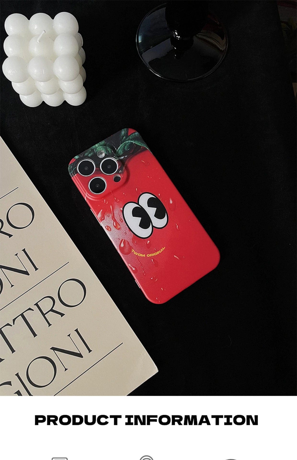 A Tomato Face iPhone 16 Pro Max Case, featuring a fun red cartoon design and offering quirky all-inclusive protection, is placed on a dark fabric surface next to a book and a spherical candle. The words "PRODUCT INFORMATION" are visible at the bottom.