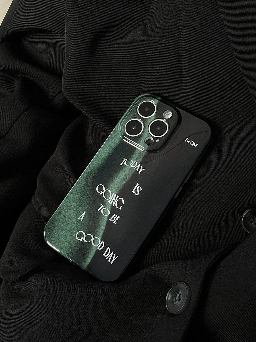 A dark-colored iPhone 16 Pro Max with a Good Day Quote iPhone 16 Pro Max Case, featuring a sleek dark green design and the phrase "Today is going to be a good day," is placed on black, buttoned fabric.