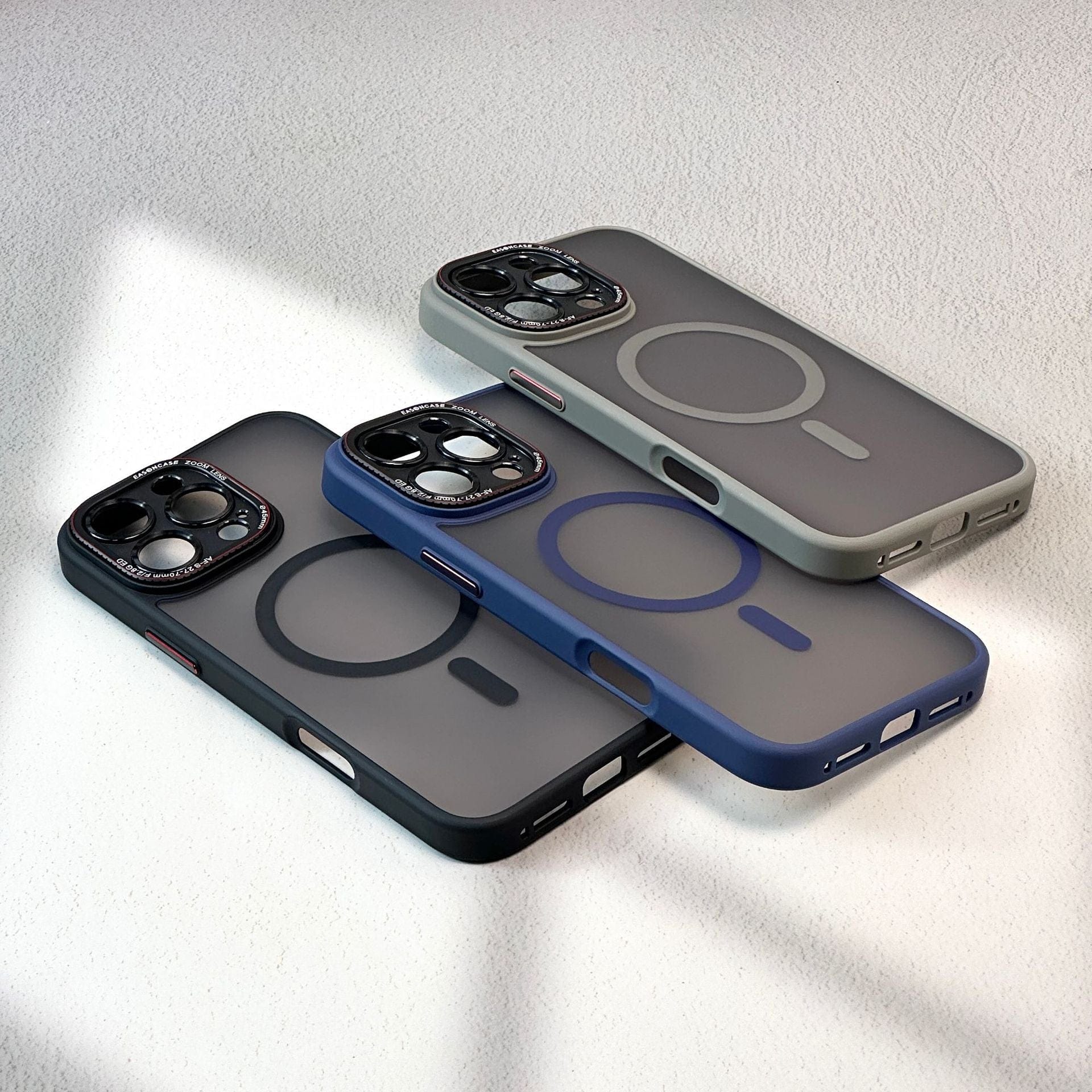 Three iPhone 16 Pro Max Cases - Matte Finish, Shockproof Full-Coverage with MagSafe Compatibility in black, gray, and blue are arranged on a smooth white surface. Each case features a transparent back with a circular design around the camera cutout.