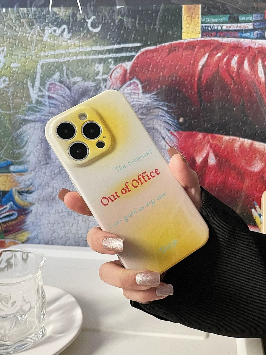 A hand with manicured nails holds the 'Out of Office' iPhone 16 Pro Max Case, featuring a gradient yellow design, in front of a background showcasing a partially completed jigsaw puzzle.