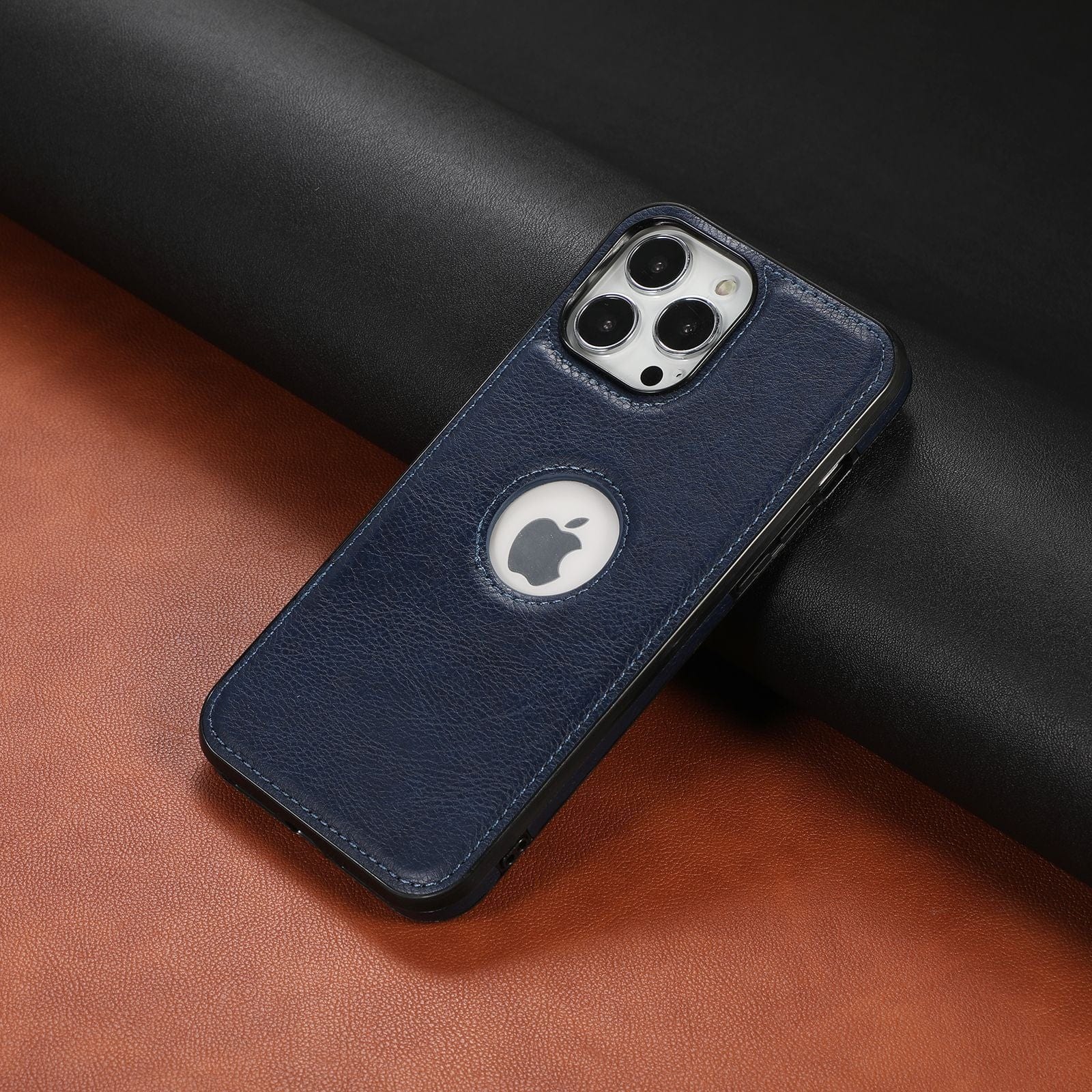 An iPhone 16 Pro Max encased in a premium synthetic leather, shockproof, anti-fingerprint protective cover with a blue finish and circular cutout around the brand logo is placed on a black and brown surface.