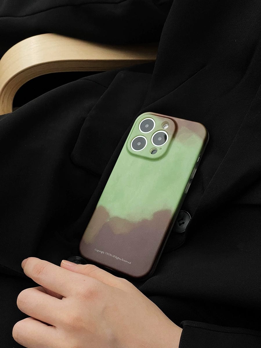 A hand resting on a person's lap is holding an iPhone 16 Pro Max with a Midnight Galaxy case featuring a cosmic starry design. The person is wearing dark-colored clothing and is seated in a light-colored wooden chair.