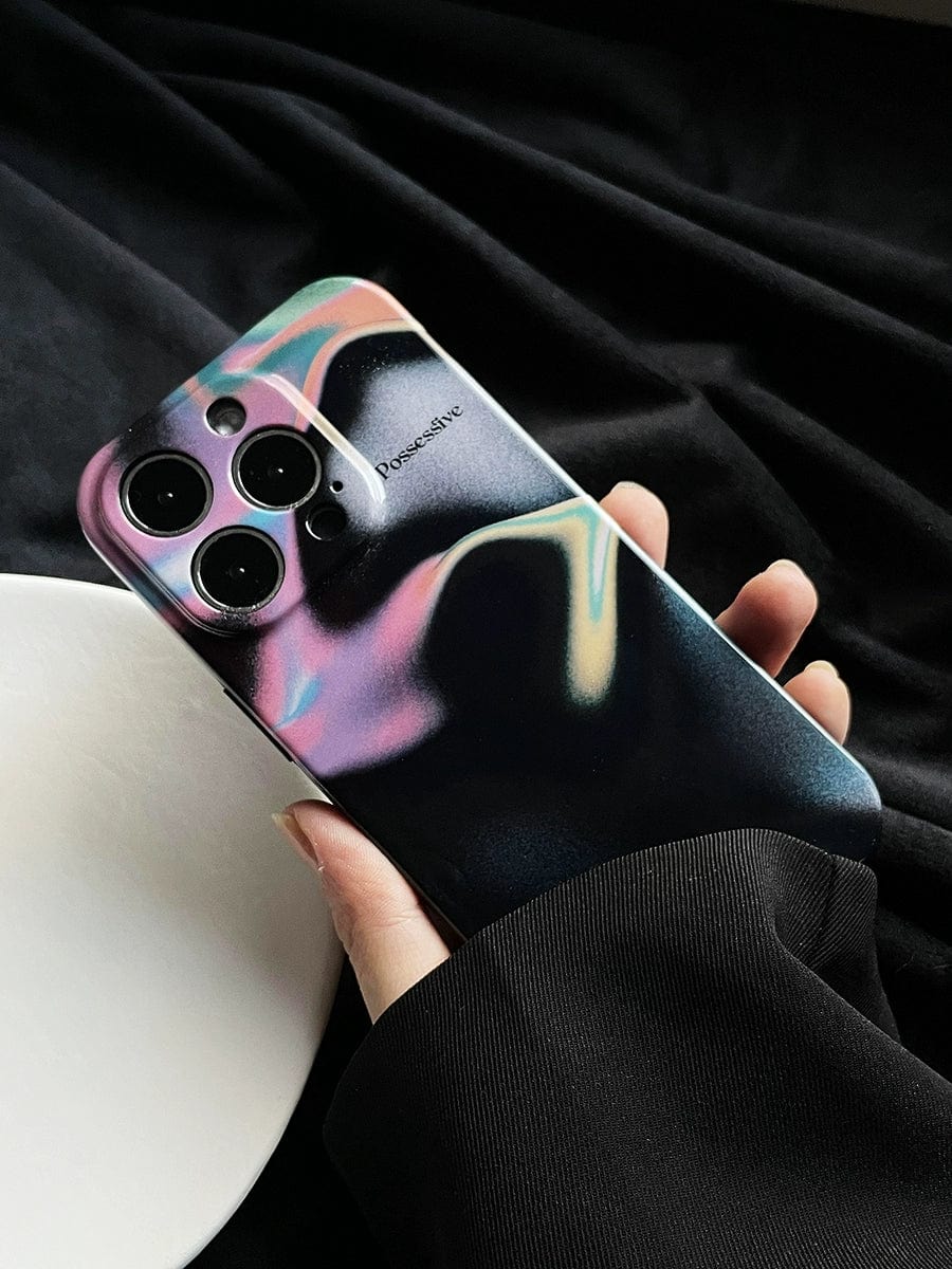 A hand holding the Possessive Aura iPhone 16 Pro Max Case featuring an abstract fluid design with a vibrant mix of pink, green, and yellow hues on a black background. The phone, equipped with three rear cameras, displays the brand name "Powerotive" prominently on the case. The backdrop is composed of dark fabric.