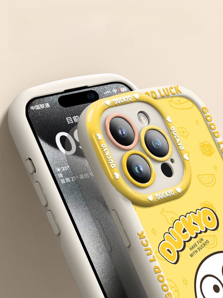 A close-up of the iPhone 16 Pro Max Yellow Duck Cartoon Case showcases a screen in Chinese and features an adorable yellow duck design. This soft liquid silicone protective cover provides shockproof protection and is adorned with cartoon ducks, the word "DUCKYO," and "GOOD LUCK" text around the edges.