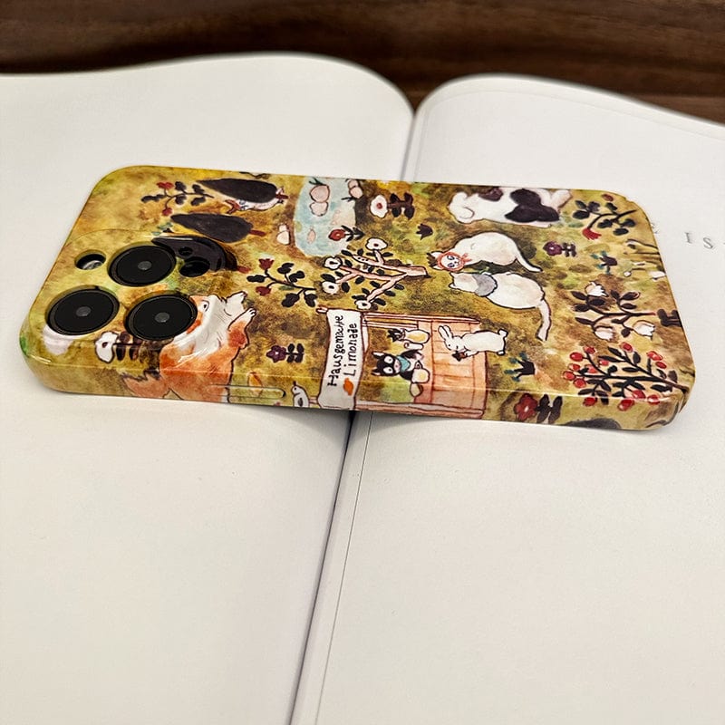 A close-up of a smartphone adorned with the Charming Forest Friends iPhone 16 Pro Max case, showcasing a whimsical animal village design. The phone, displaying various illustrated animals in different poses, is resting on an open book with blurred text, suggesting a cozy and artistic setting.