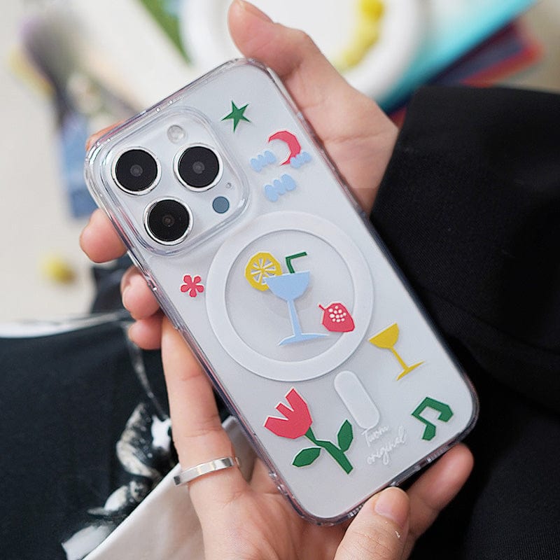 A hand holds an iPhone 16 Pro Max encased in a Tropical Vibes MagSafe Case, which features colorful, raised 3D elements including drinks, a flower, a moon, and musical notes. The phone has three camera lenses.