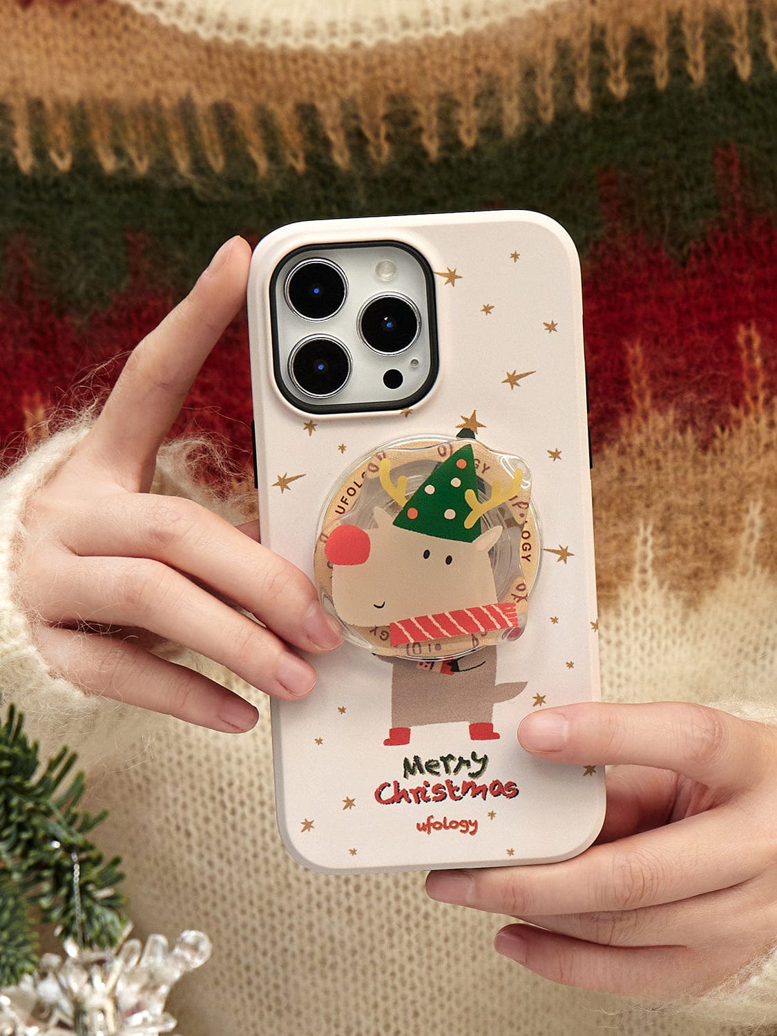 Hands holding a Rudolph Joy MagSafe iPhone 16 Pro Max Case, adorned with a festive reindeer design and the words "Merry Christmas.