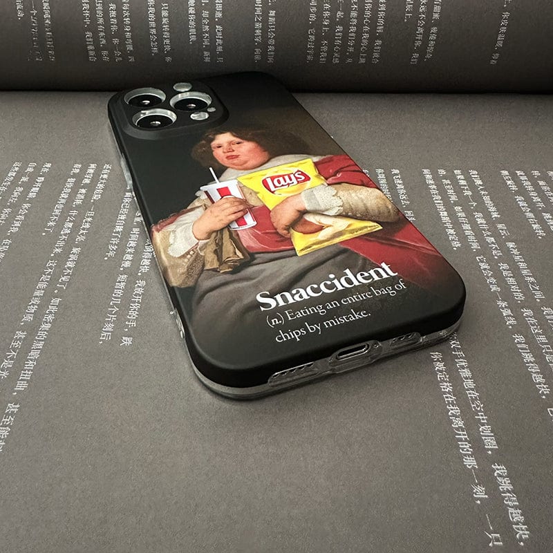 The Snaccident iPhone 16 Pro Max Case features a classical painting of a person in historical attire holding a soft drink and a bag of Lay’s chips, with the text: "Snaccident (n.) Eating an entire bag of chips by mistake." The phone is placed on an open book.