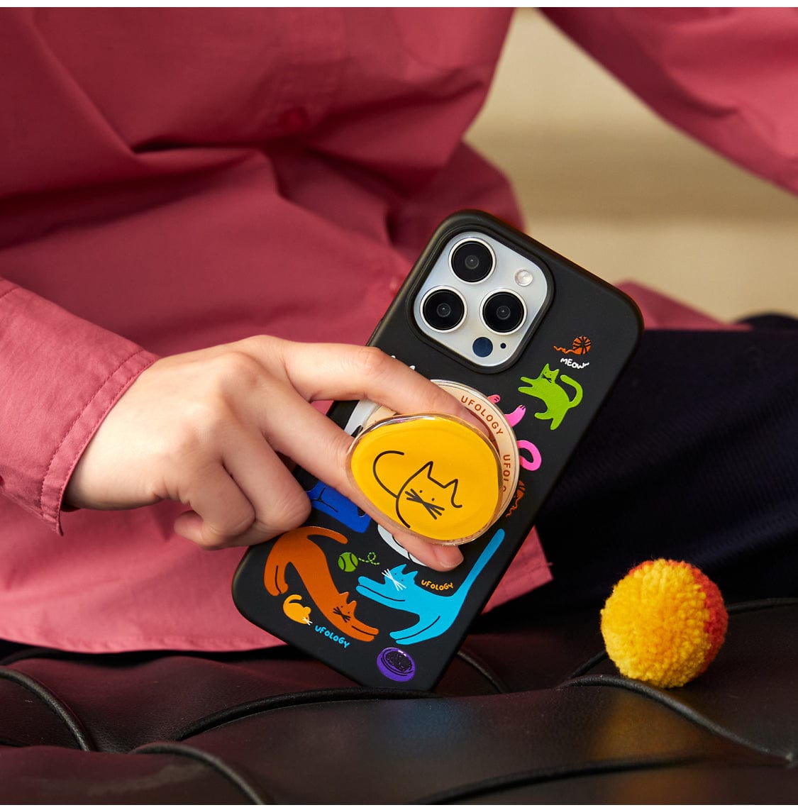 A hand is holding the Colorful Cats MagSafe iPhone 16 Pro Max Case, which boasts a vibrant design featuring various cat illustrations and includes an all-inclusive protective cover with a cat stand.