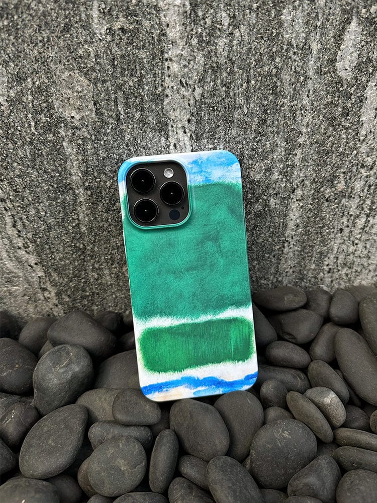 An iPhone 16 Pro Max adorned with the Abstract Color Block case, featuring a modern art-inspired, minimalist design in shades of green and blue, rests against a rough-textured gray stone wall. The smartphone, showcasing its high-quality design and full protection case, is surrounded by smooth, dark stones.