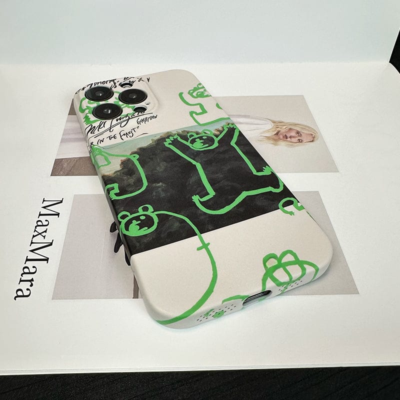 An iPhone 16 Pro Max adorned with the Unique Green Bear Graphic Case, which showcases a creative forest art design featuring green cartoon animals, including a prominent central bear and various smaller creatures in white and black. The ultra-slim, full-edge protective case rests on an open book displaying a black-and-white photograph of a woman along with the word "MaxMara.