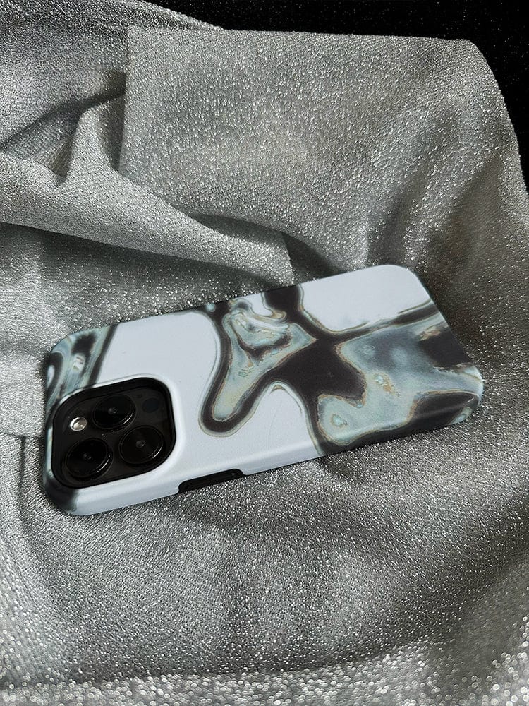 The Abstract Metallic Flow iPhone 16 Pro Max Case, showcasing a sleek modern art design in shades of gray and black, rests on a silver, shimmery fabric. The phone is positioned with its camera lenses facing up.