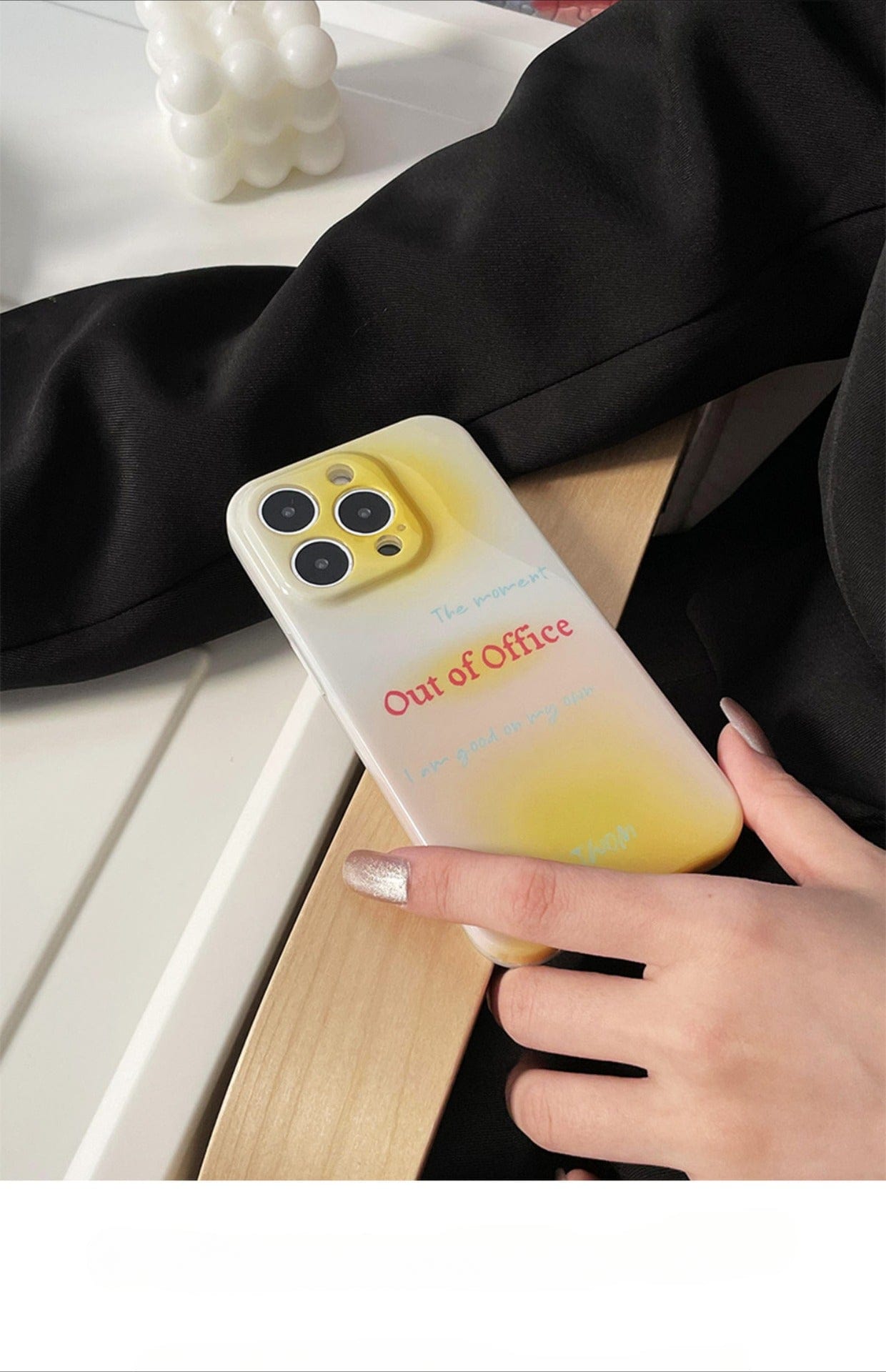 A hand holding an iPhone 16 Pro Max with an Out of Office iPhone 16 Pro Max Case featuring a gradient yellow design and text saying, "The Manager is Out of Office, I am Out of my Mind." The hand is resting on a wooden surface.