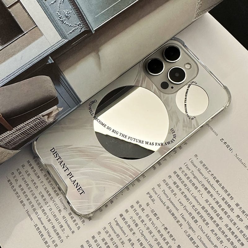 A mirror-finished smartphone with a Futuristic Distant Planet iPhone 16 Pro Max Case displaying reflective circular designs and text lies on an open magazine with articles and images. The case bears phrases such as "DISTANT PLANET" and "WHEN IT BECAME SO BIG THE FUTURE WAS FAR AWAY.